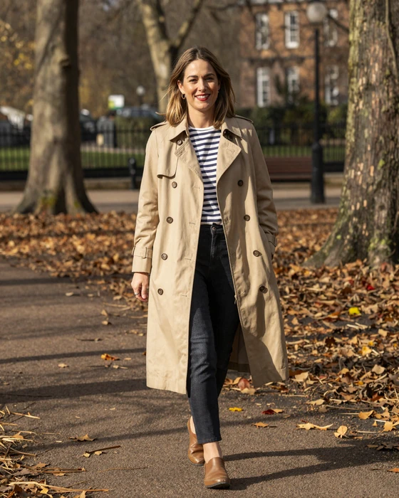 Stylish British woman in trench coat walking through London park in autumn