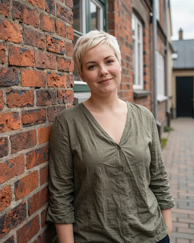 Ida a 34-year-old Danish woman with short platinum blonde hair smiling in a charming Danish alley