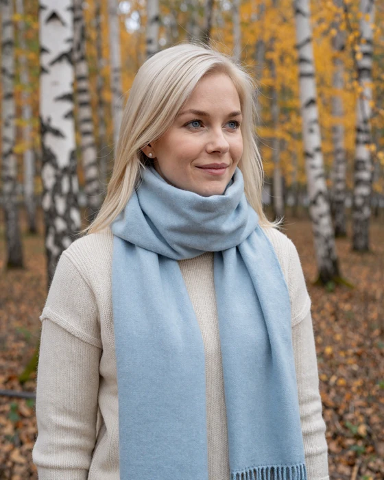 Finnish woman with platinum blonde hair smiling near birch forest in autumn wearing cozy cream sweater