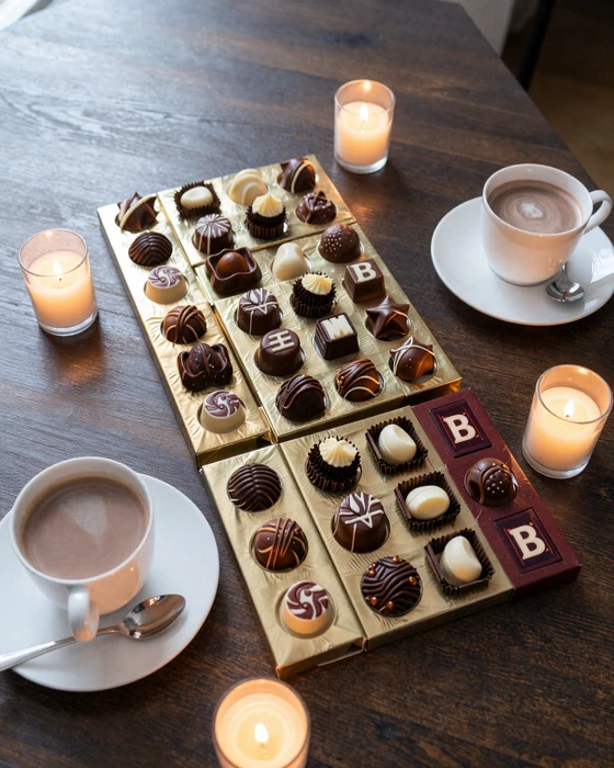 Artisan Belgian chocolate and praline display with hot chocolate cups in romantic candlelight setting